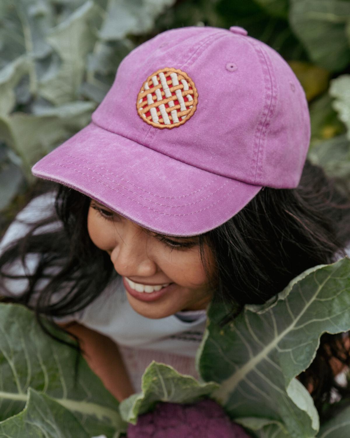 Person wearing a pink cap with a circular patch in a garden setting