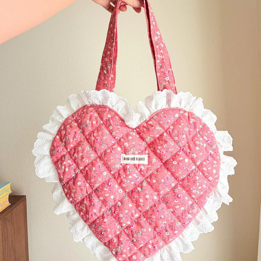 Heart-shaped pink bag with white ruffles held by a hand against a beige background