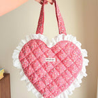 Heart-shaped pink bag with white ruffles held by a hand against a beige background