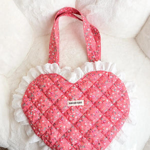 Heart-shaped pink bag with ruffled edge and floral handle on a white background