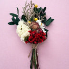 Bouquet of flowers with red, white, and green elements on a pink background