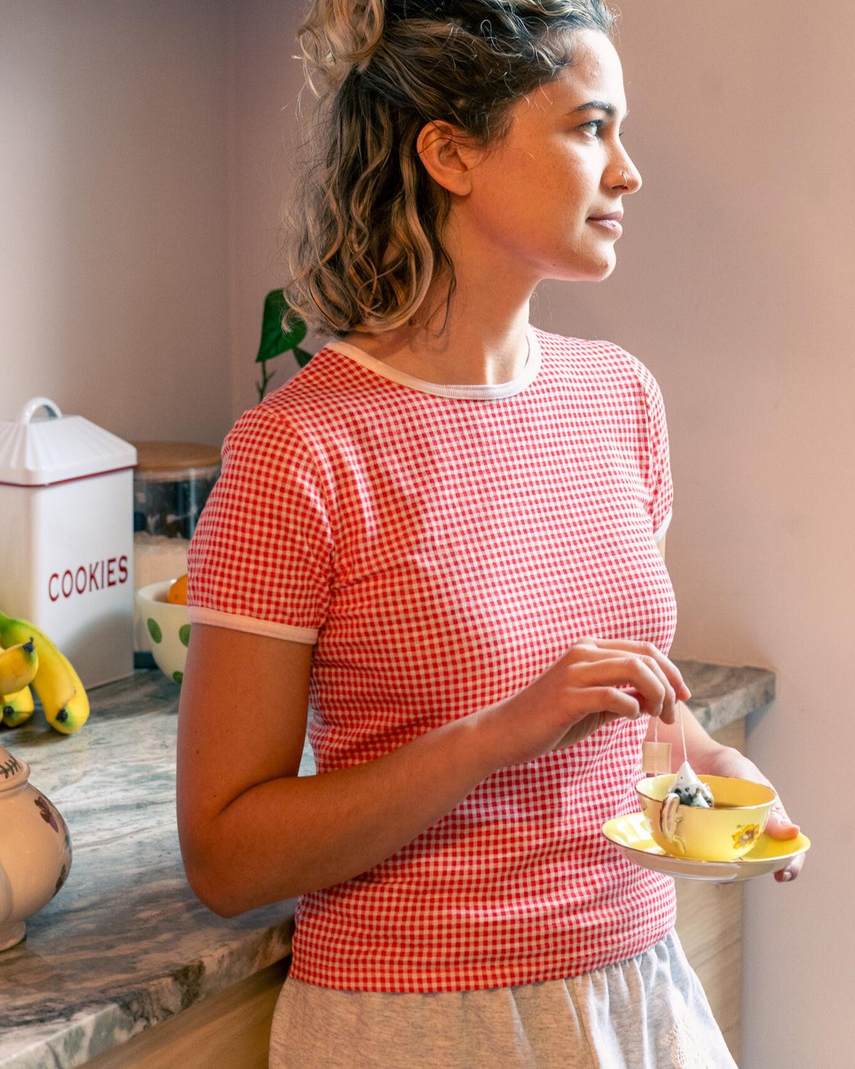 Woman in a red checkered shirt holding a small plate with a dessert in a kitchen.