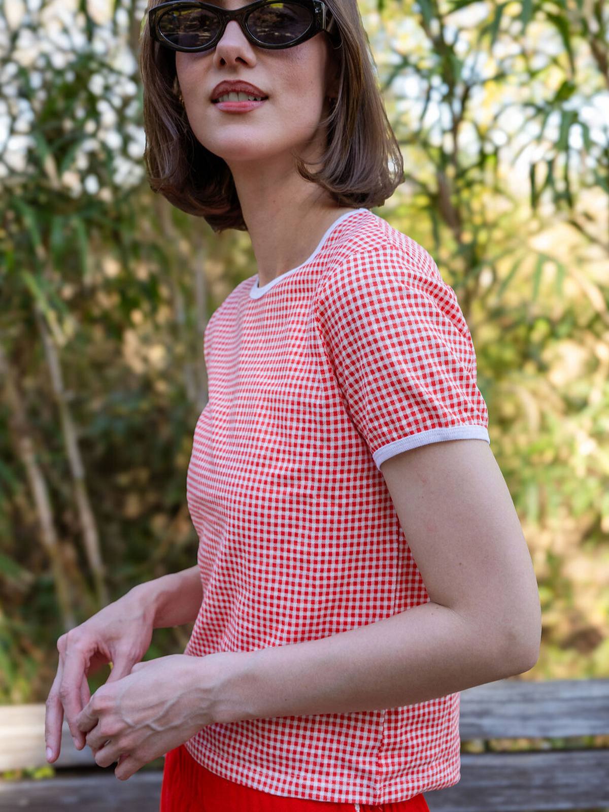 Woman wearing a red and white checkered shirt with sunglasses outdoors.