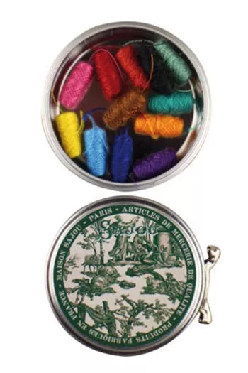 Colorful spools of thread in a metal tin with decorative green and white lid on a white background