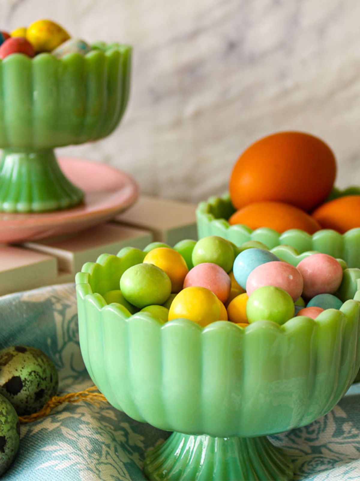 Green glass bowl filled with colorful Easter eggs on a patterned surface.