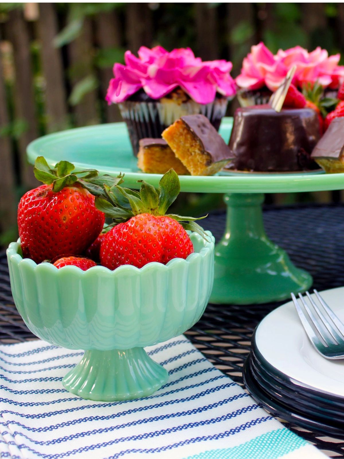 Mint green bowl with strawberries on a table with cake and flowers in the background