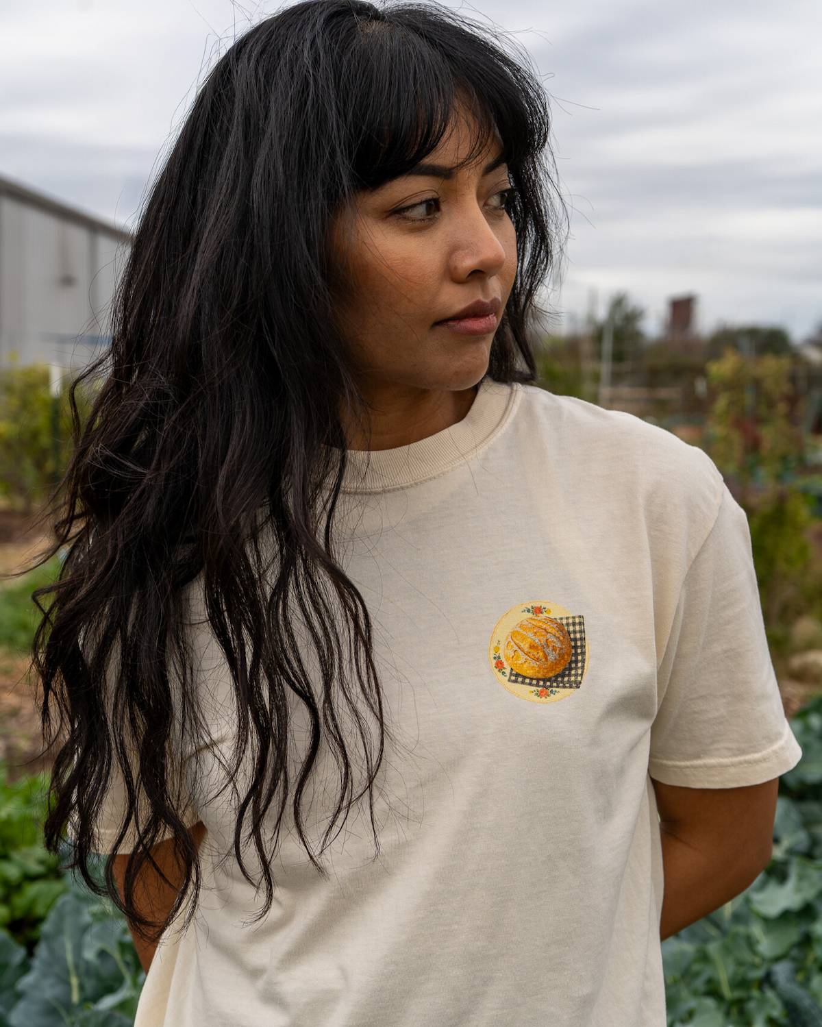 Person wearing a white t-shirt with a small graphic on it, standing in an outdoor setting.