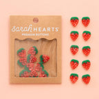 Packaging of strawberry-shaped buttons with 'sarahHEARTS' branding on a pink background.
