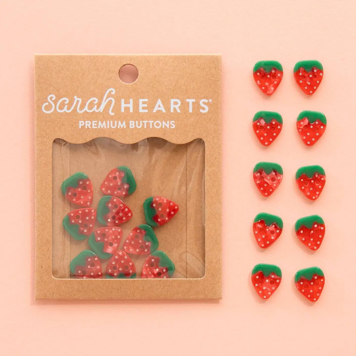 Packaging of strawberry-shaped buttons with 'sarahHEARTS' branding on a pink background.