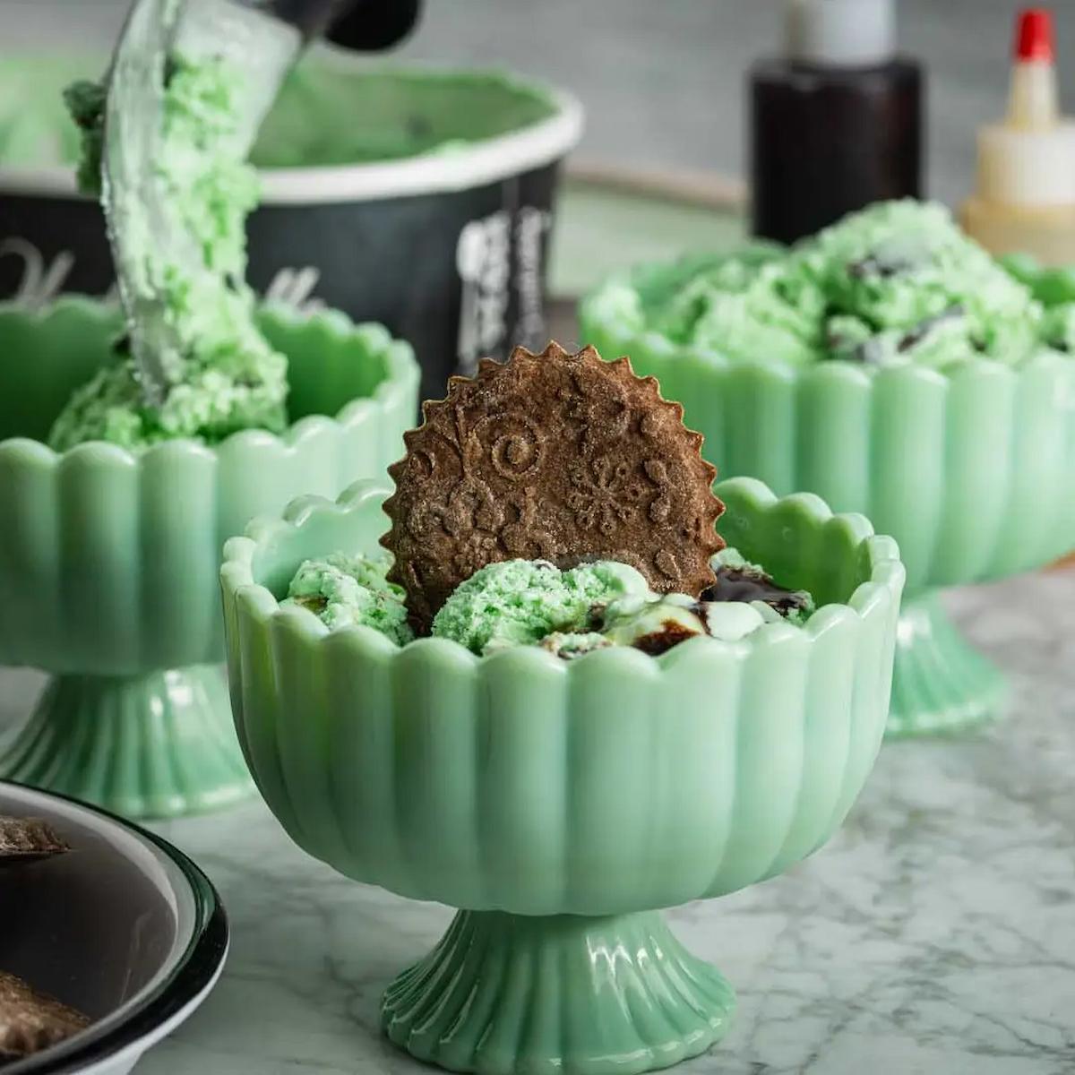 Green ceramic bowl with a cookie and green dessert, set on a marble surface.