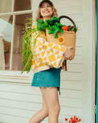 Woman holding a woven basket with groceries and a patterned jacket in front of a white door.