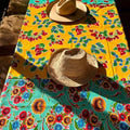Colorful floral-patterned tablecloth with two straw hats on a wooden surface.