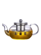 Clear glass teapot with metal lid and handle filled with tea on a white background