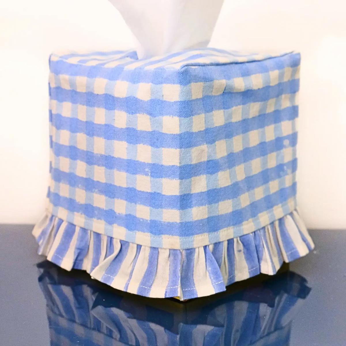 Blue and white checkered ottoman with ruffled edge on a reflective surface.