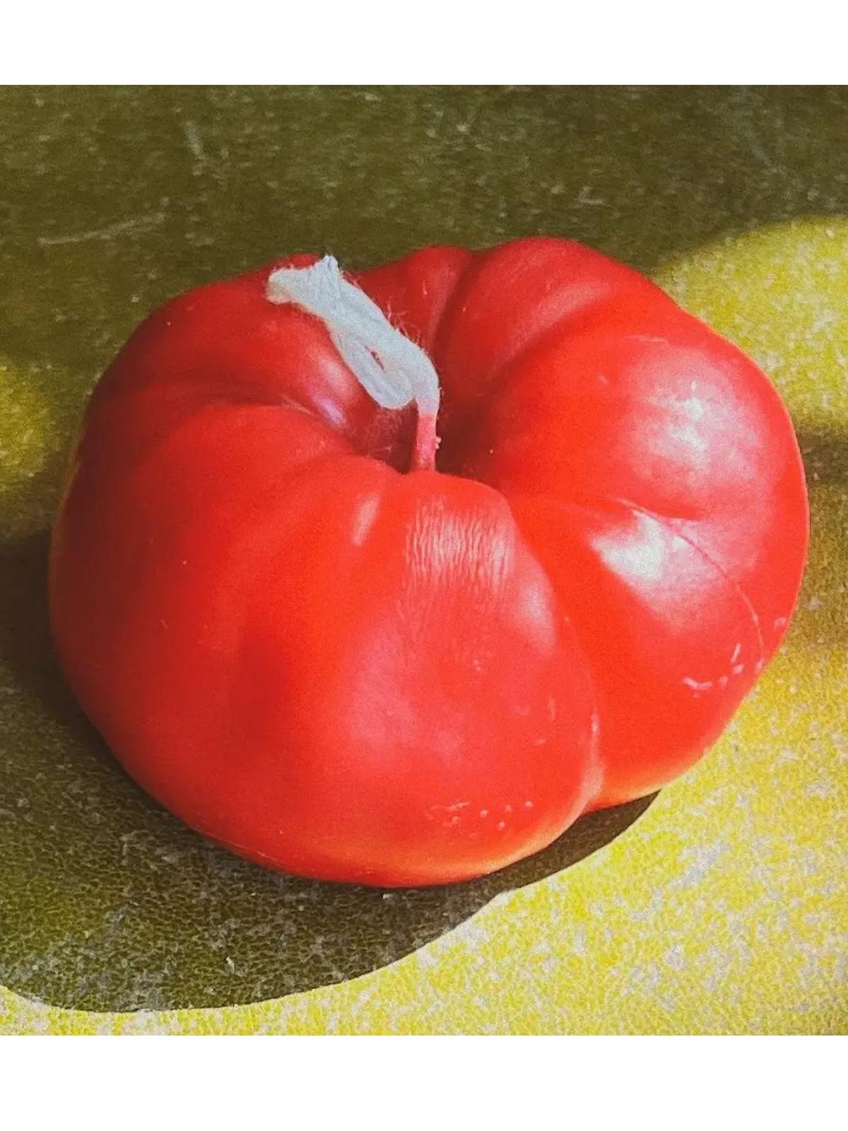 Red candle shaped like a fruit on a textured green and yellow background