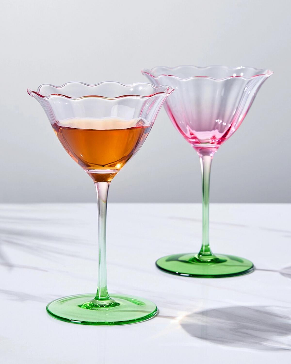 Two cocktail tulip shaped glasses with green colored base on a white surface
