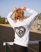 Person on an outdoor athletic track wearing a white sweatshirt with a large black heart-shaped graphic on the back, paired with black track pants.