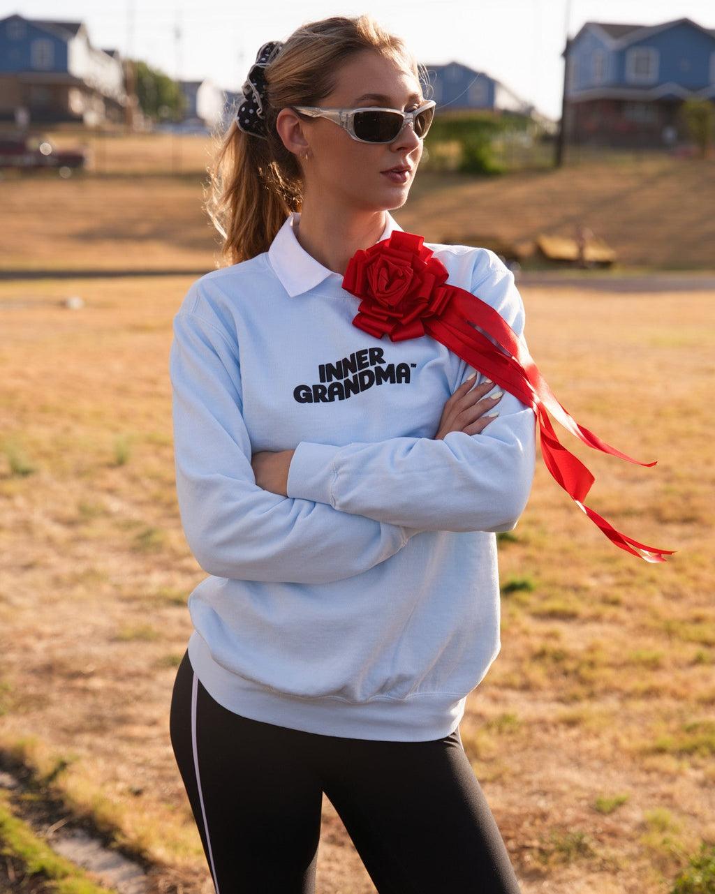 Person wearing a light blue crewneck sweatshirt with a white collar and the words 'INNER GRANDMA' printed in black, accessorized with a large red rose brooch. 