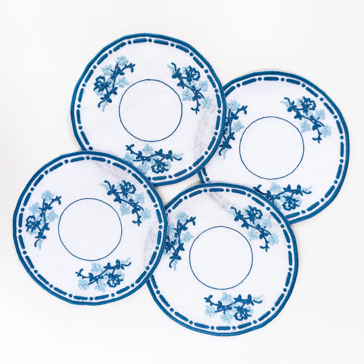 Four blue and white decorative cocktail coasters with floral patterns on a white background