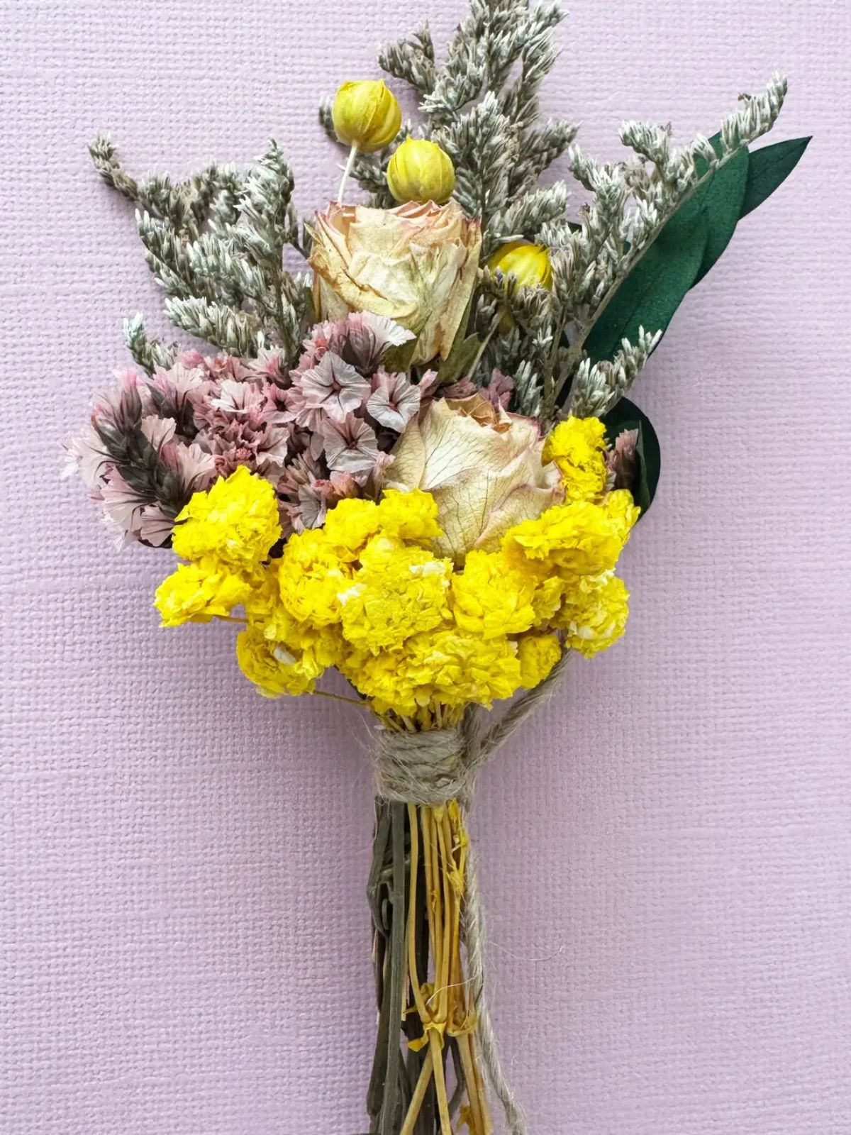 Bouquet of dried flowers with yellow, pink, and green elements on a light purple background